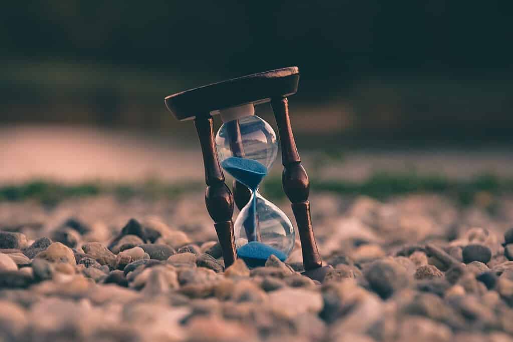 A timeless hourglass with blue sand stands in a bed of stones, representing the age-old question of 'how long does it take to learn French?' While it may seem like a daunting task, with the right resources and dedication, you can master the language relatively quickly.