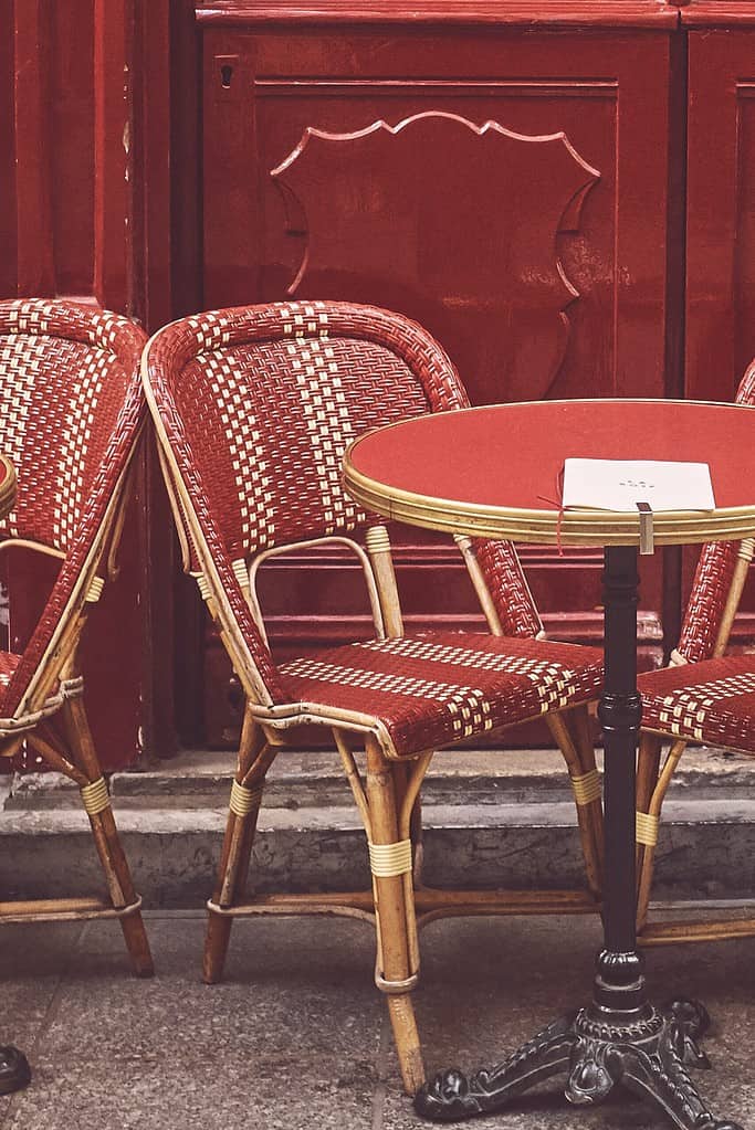 Enjoy a French conversation learning session outdoors in the sunshine with a steaming cup of coffee on the small round table, surrounded by vibrant red chairs. A perfect setting to practice your French and make lasting memories.
