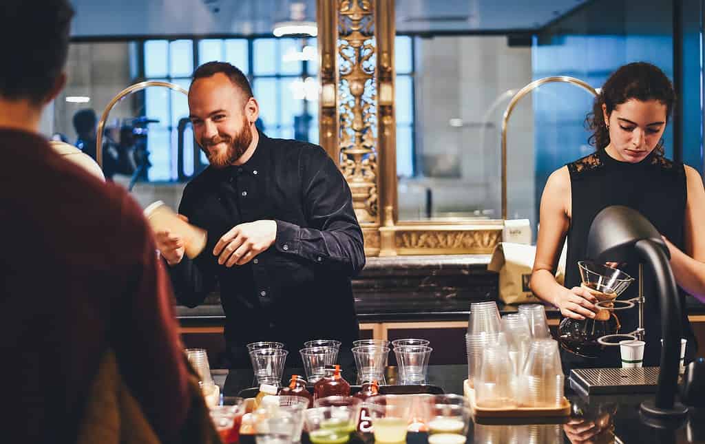 Deux barmans préparant des cocktails tout en améliorant leur 'anglais conversationnel accueil' pour mieux servir les clients internationaux.
