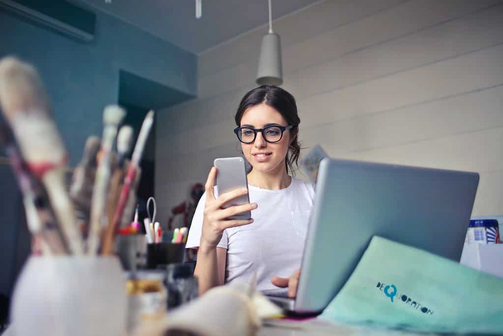Une jeune femme utilisant l'application apprendre anglais sur son téléphone tout en étant assise devant son ordinateur portable.