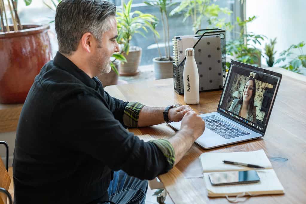 Un homme d'âge moyen en chemise noire engage une 'conversation anglais en ligne' avec une femme via Zoom, illustrant l'efficacité des appels vidéo pour l'apprentissage et l'amélioration des compétences en anglais.