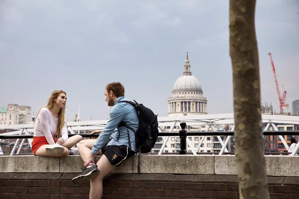 Un homme et une femme s'engageant dans une 'conversation en anglais' assis sur un mur près de la Tamise, avec la cathédrale Saint-Paul en arrière-plan.